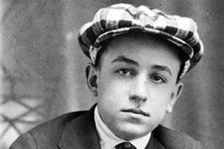 Retrato em preto e branco de um garoto com boné xadrez, vestindo um terno, olhando para a câmera.