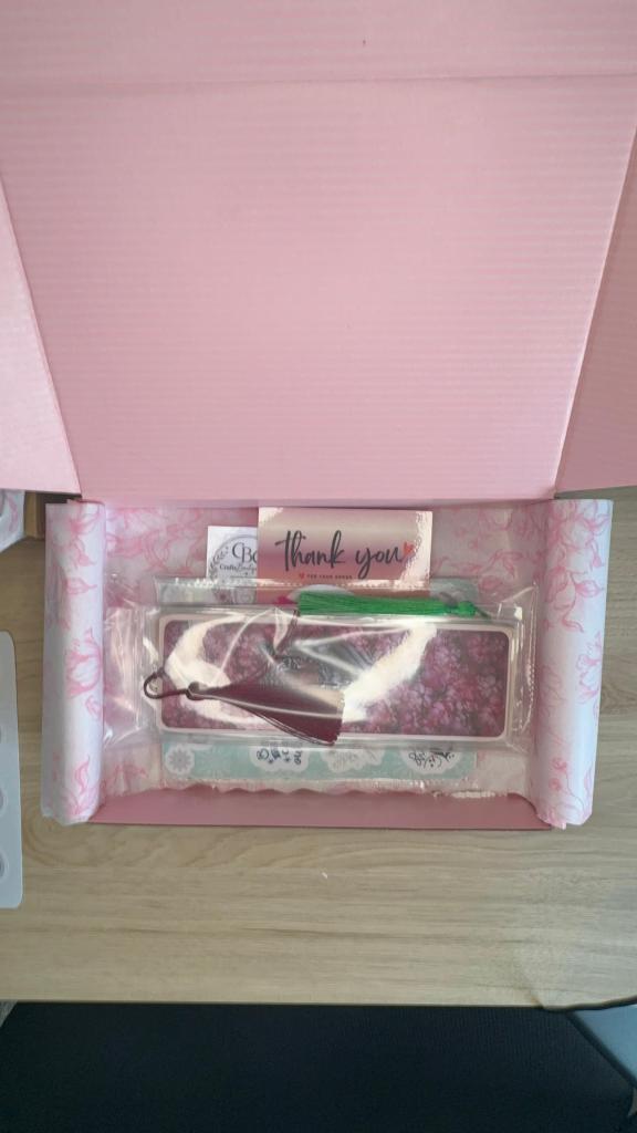 Caixa rosa aberta com um bilhete 'Thank you' e itens embalados, incluindo um porta-objetos decorado e papel de seda.